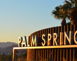 A sign that says palm springs in front of the mountains.